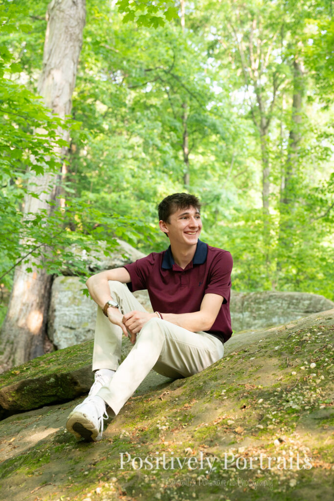 Whipps Ledges Hinckley Ohio Senior Photos Brunswick Ohio. Senior boy wearing firefighter jacket and helmet on rocky ledge at Whipps Ledges with forest backdrop, symbolizing future career and strength