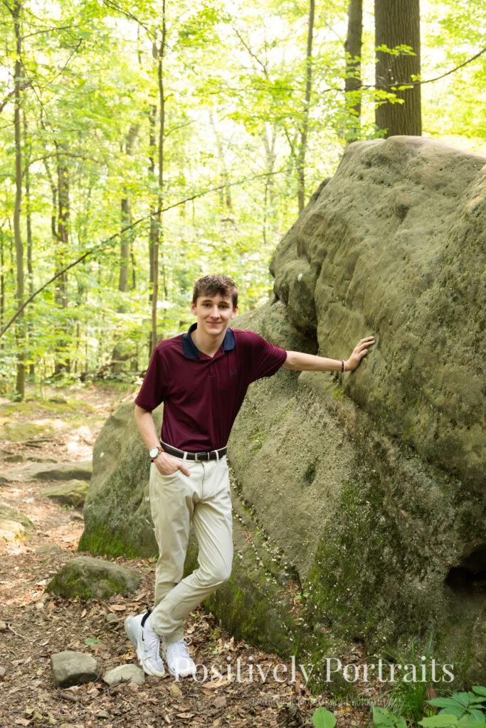Whipps Ledges Hinckley Ohio Senior Photos Brunswick Ohio. Senior boy wearing firefighter jacket and helmet on rocky ledge at Whipps Ledges with forest backdrop, symbolizing future career and strength