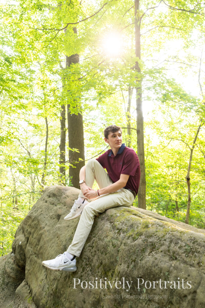 Whipps Ledges Hinckley Ohio Senior Photos Brunswick Ohio. Senior boy wearing firefighter jacket and helmet on rocky ledge at Whipps Ledges with forest backdrop, symbolizing future career and strength