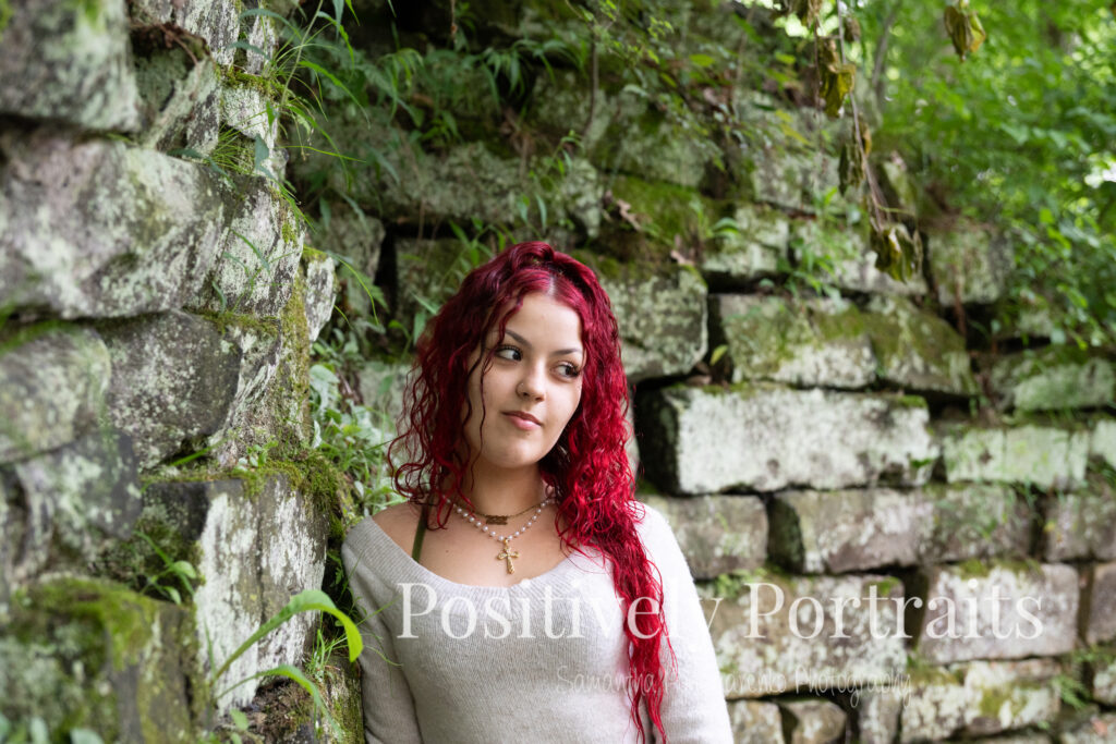 Jocelyn poses confidently on a large rock above the Rocky River at David Fortier River Park in Olmsted Falls, Ohio, wearing a black skirt and gray sweater, surrounded by flowing water and lush greenery. Her senior portraits capture both elegance and adventure, with additional images highlighting stone textures, ivy-covered walls, and classic architecture. The session includes a bold look with a black dress and leopard heels, and ends with cap and gown photos by the riverside, celebrating her graduation.
