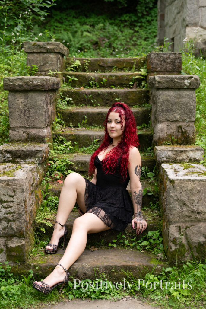 Jocelyn poses confidently near the Rocky River at David Fortier River Park in Olmsted Falls, Ohio by flowing water and lush greenery. Her senior portraits capture both elegance and adventure, with additional images highlighting stone textures, ivy-covered walls, and classic architecture. The session includes a bold look with a black dress and leopard heels, and ends with cap and gown photos by the riverside, celebrating her graduation.
