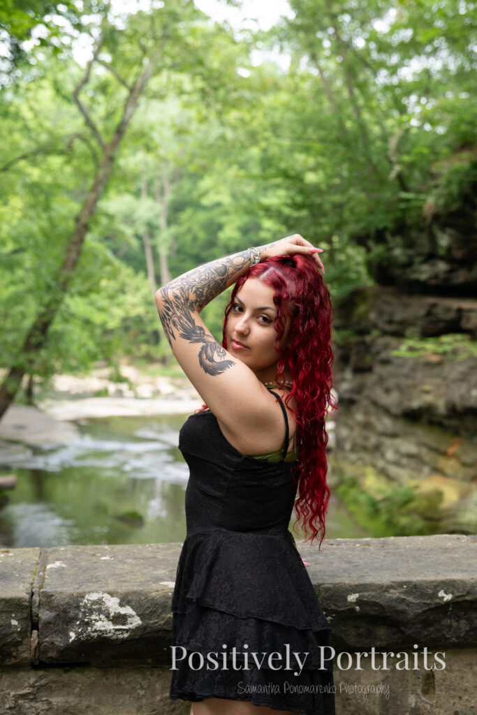 Jocelyn poses confidently near the Rocky River at David Fortier River Park in Olmsted Falls, Ohio by flowing water and lush greenery. Her senior portraits capture both elegance and adventure, with additional images highlighting stone textures, ivy-covered walls, and classic architecture. The session includes a bold look with a black dress and leopard heels, and ends with cap and gown photos by the riverside, celebrating her graduation.