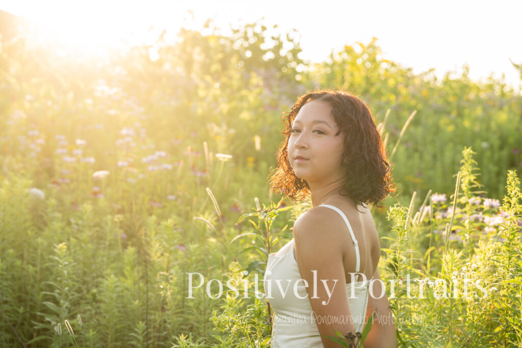 Emerson standing in a field of wildflowers at Brunswick Lake Park, early morning sunlight creating a dreamy glow around her.