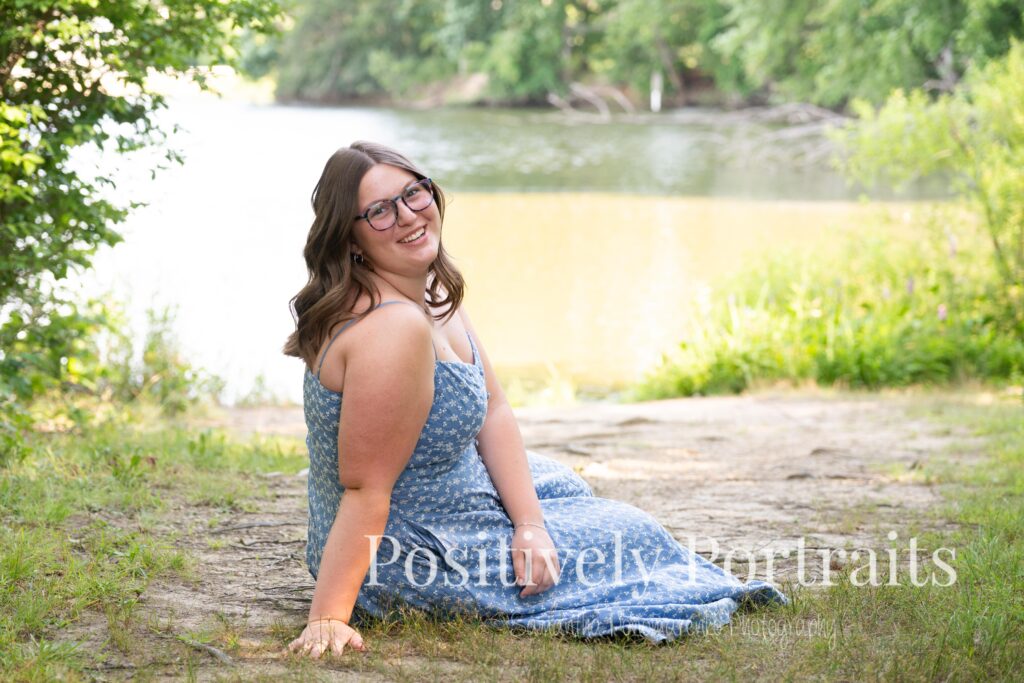 Senior portraits of Tabitha in a blue floral dress on a tree-lined path at Brunswick Lake, golden sunlight filtering through the leaves.