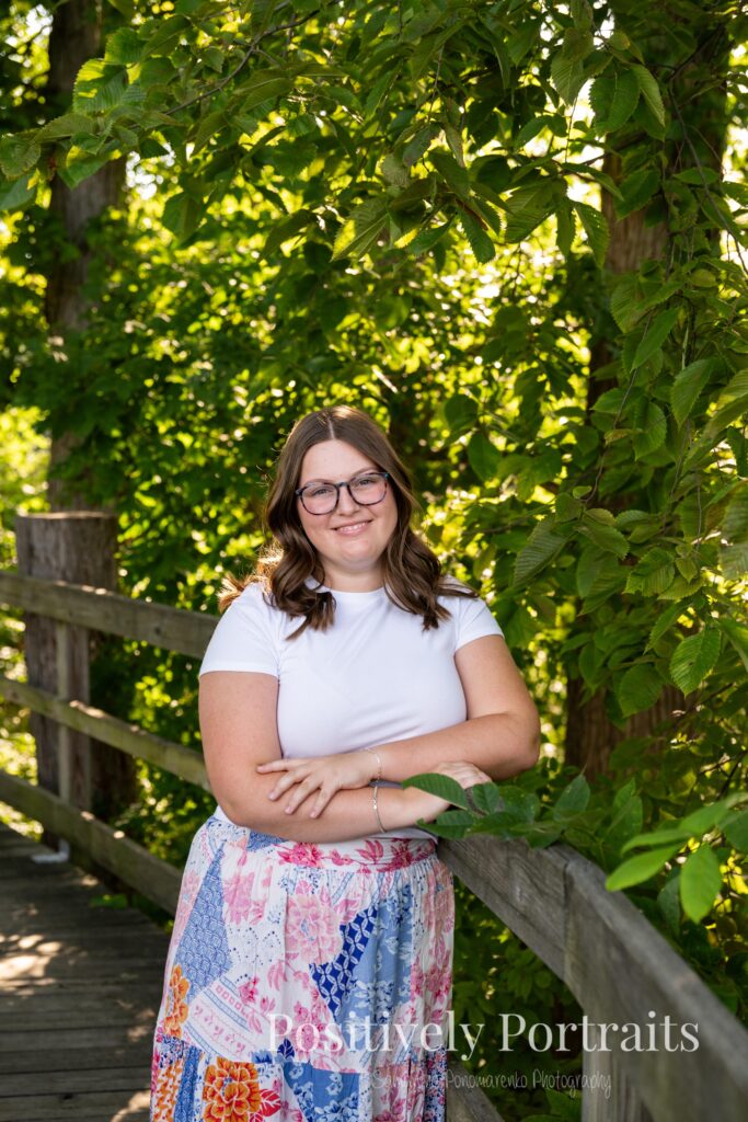 Tabitha in a white t-shirt and colorful patchwork skirt standing on a wooded trail at Brunswick Lake, her outfit’s vibrant patterns contrasting with the greenery.