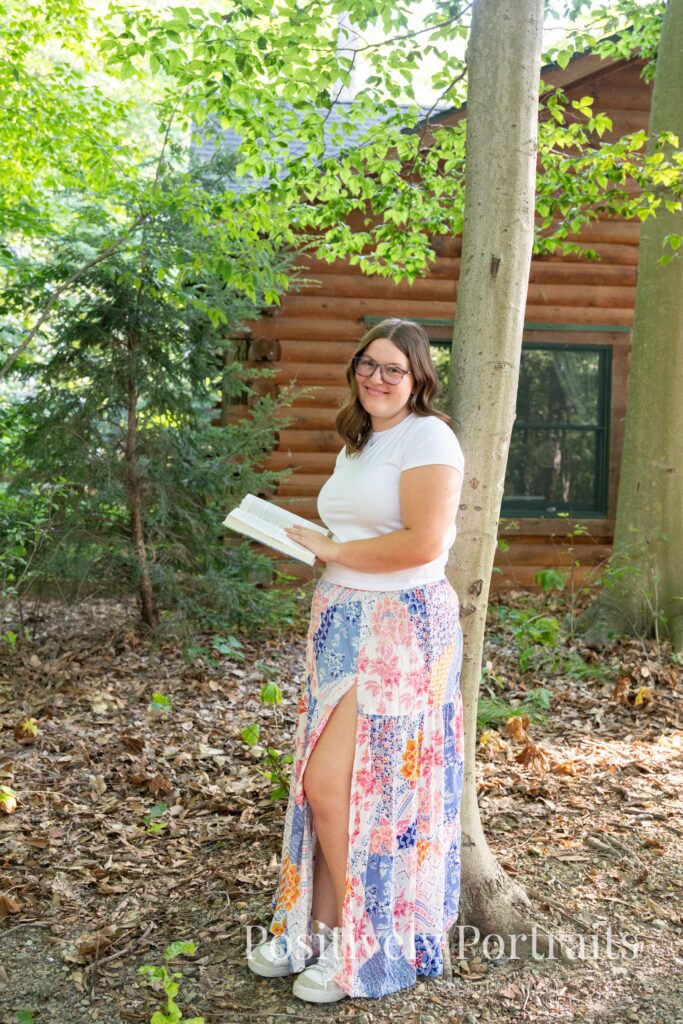 Tabitha in a white t-shirt and colorful patchwork skirt standing on a wooded trail at Brunswick Lake, her outfit’s vibrant patterns contrasting with the greenery.