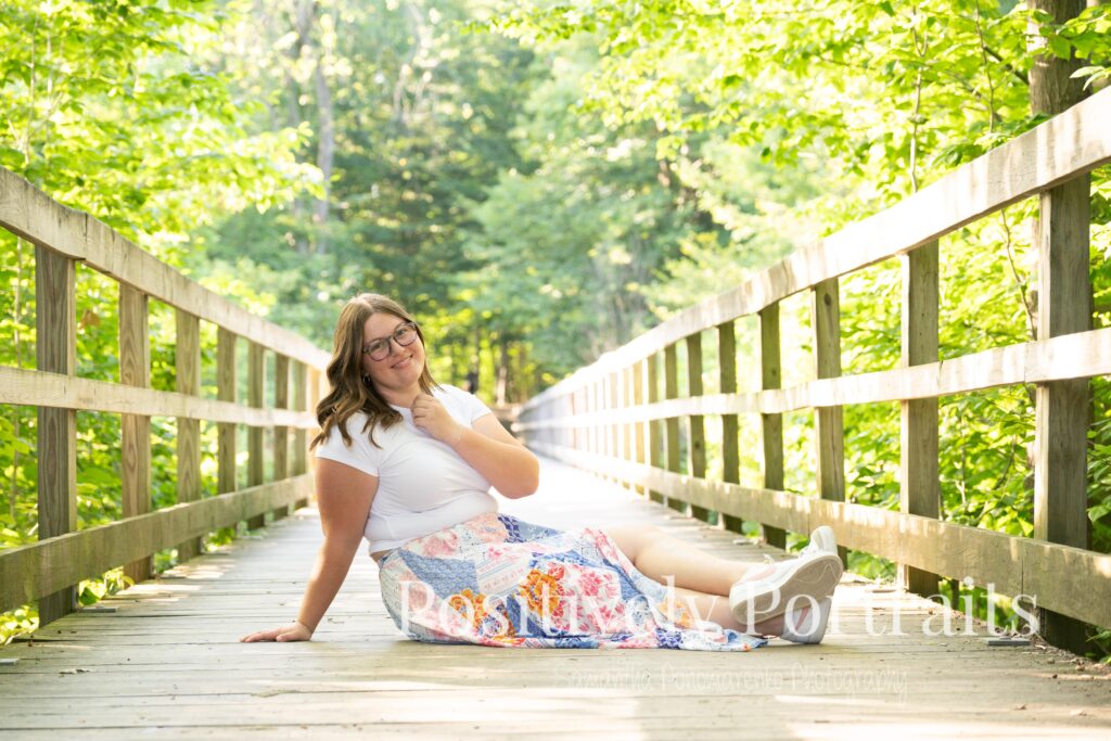 Tabitha in a white t-shirt and colorful patchwork skirt standing on a wooded trail at Brunswick Lake, her outfit’s vibrant patterns contrasting with the greenery.