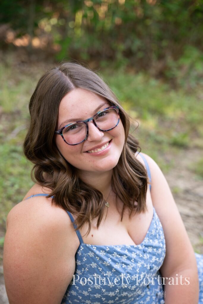 Senior portraits of Tabitha in a blue floral dress on a tree-lined path at Brunswick Lake, golden sunlight filtering through the leaves.