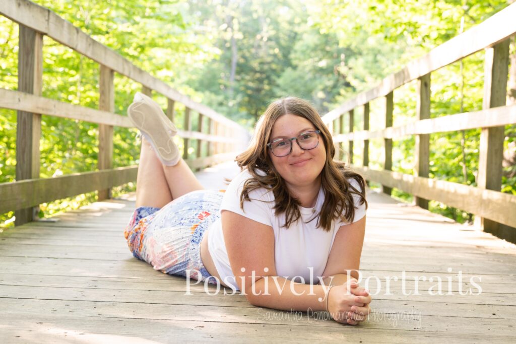 Tabitha in a white t-shirt and colorful patchwork skirt standing on a wooded trail at Brunswick Lake, her outfit’s vibrant patterns contrasting with the greenery.