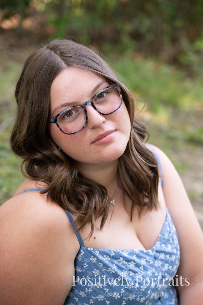 Senior portraits of Tabitha in a blue floral dress on a tree-lined path at Brunswick Lake, golden sunlight filtering through the leaves.
