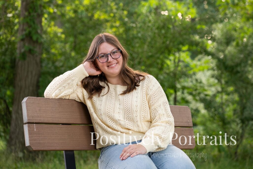 Tabitha standing by the lake’s edge at Brunswick Lake with soft ripples in the water, wearing a yellow sweater and jeans for her senior photos.