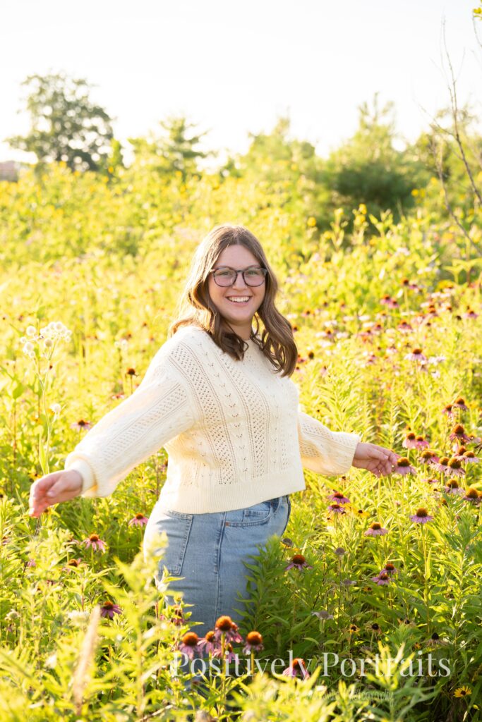 Tabitha standing by the lake’s edge at Brunswick Lake with soft ripples in the water, wearing a yellow sweater and jeans for her senior photos.
