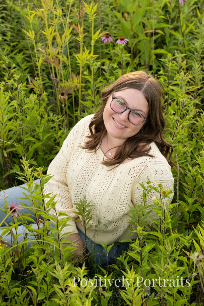Tabitha standing by the lake’s edge at Brunswick Lake with soft ripples in the water, wearing a yellow sweater and jeans for her senior photos.