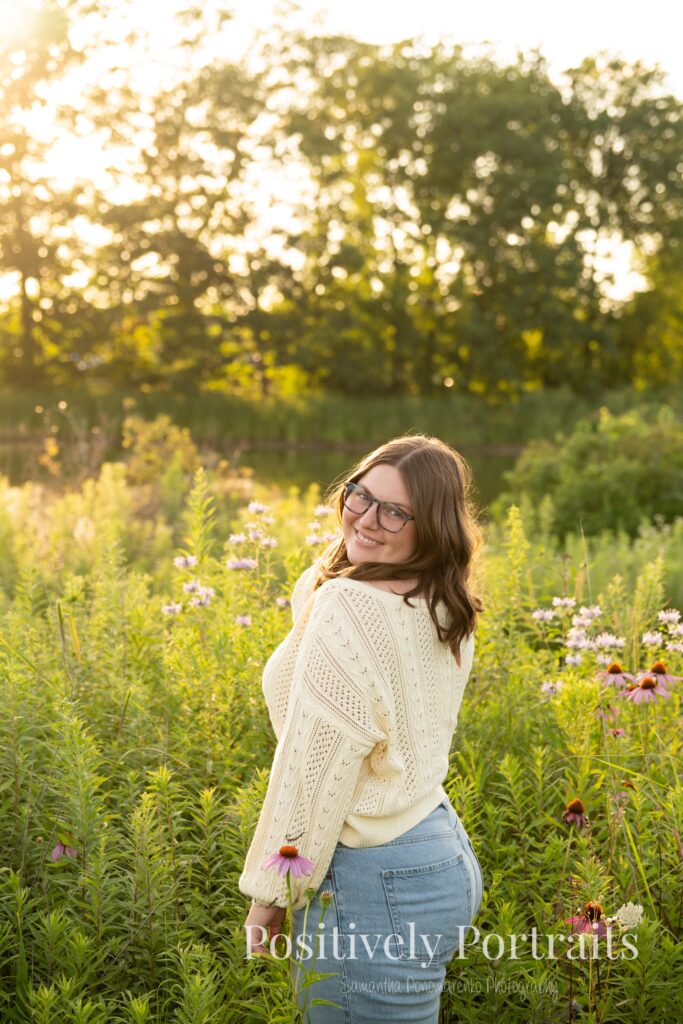 Tabitha standing by the lake’s edge at Brunswick Lake with soft ripples in the water, wearing a yellow sweater and jeans for her senior photos.