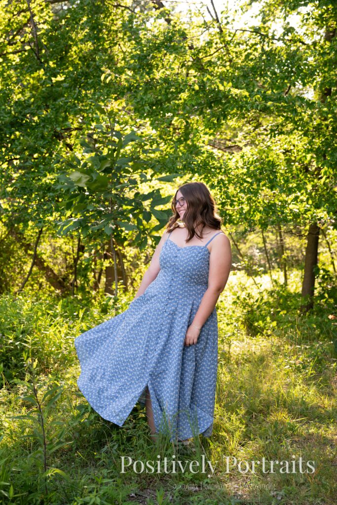 Senior portraits of Tabitha in a blue floral dress on a tree-lined path at Brunswick Lake, golden sunlight filtering through the leaves.