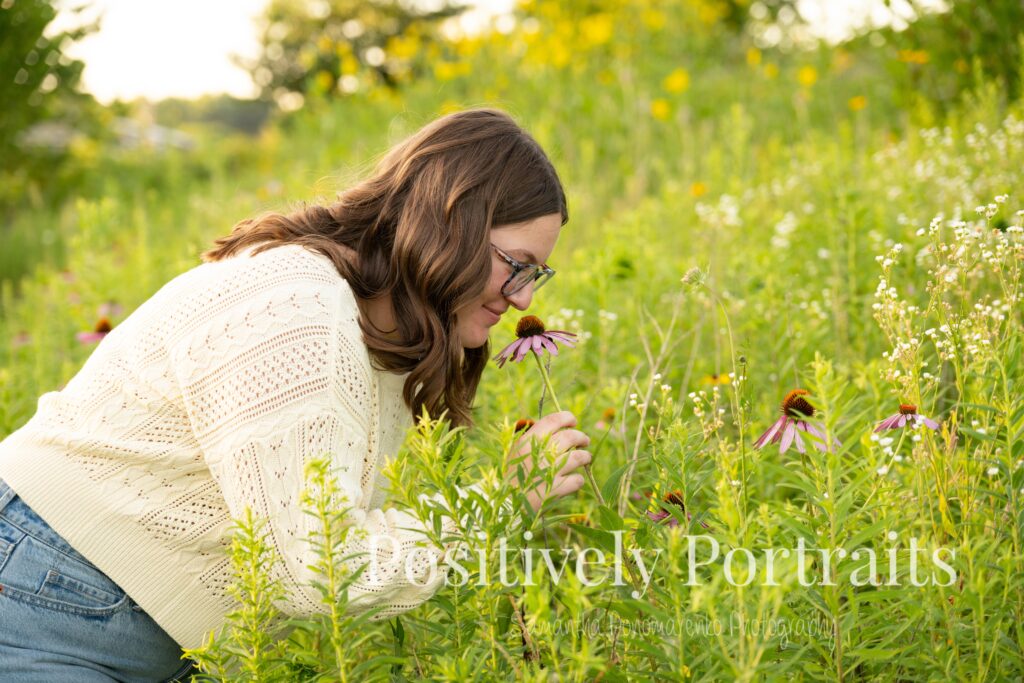 Tabitha standing by the lake’s edge at Brunswick Lake with soft ripples in the water, wearing a yellow sweater and jeans for her senior photos.