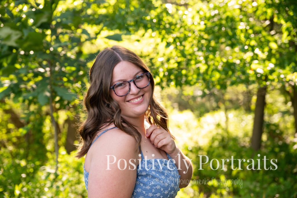 Senior portraits of Tabitha in a blue floral dress on a tree-lined path at Brunswick Lake, golden sunlight filtering through the leaves.