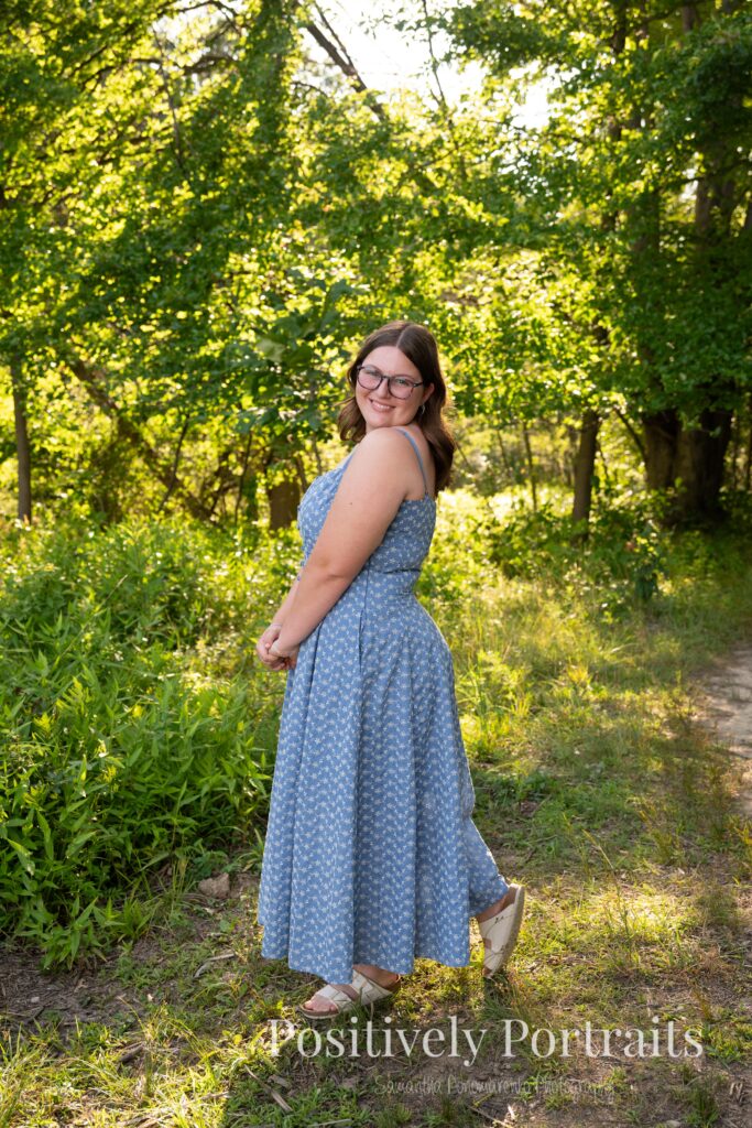 Senior portraits of Tabitha in a blue floral dress on a tree-lined path at Brunswick Lake, golden sunlight filtering through the leaves.