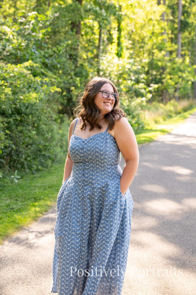 Senior portraits of Tabitha in a blue floral dress on a tree-lined path at Brunswick Lake, golden sunlight filtering through the leaves.