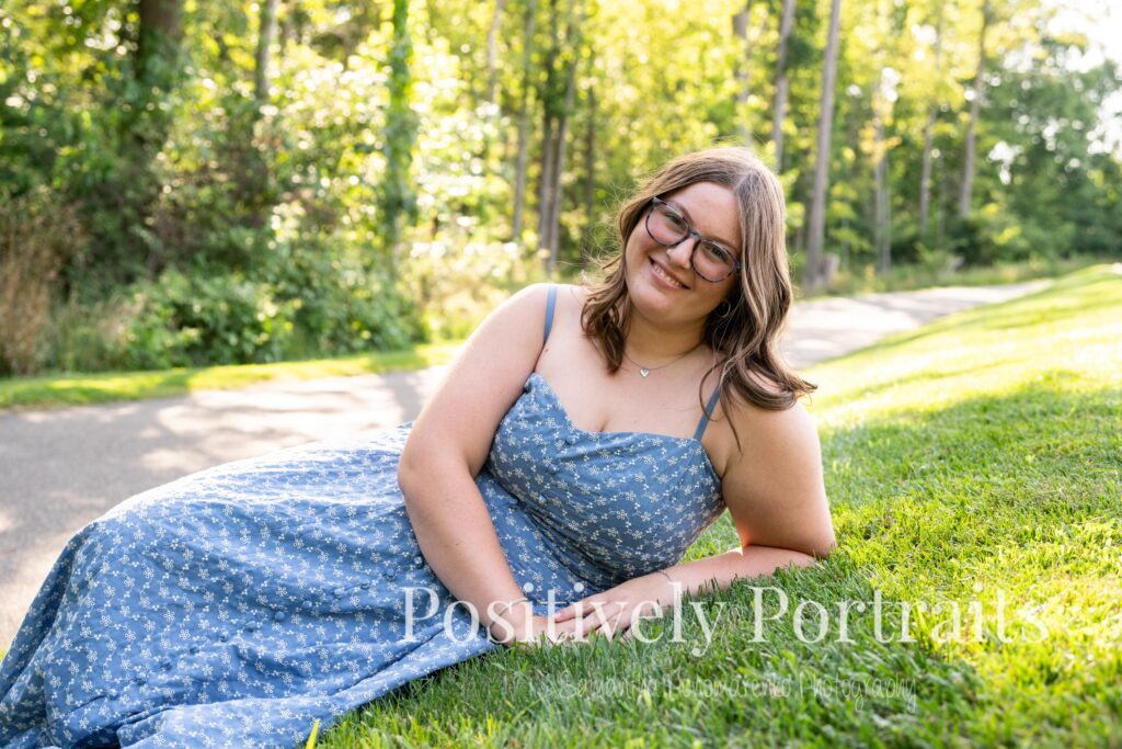 Senior portraits of Tabitha in a blue floral dress on a tree-lined path at Brunswick Lake, golden sunlight filtering through the leaves.