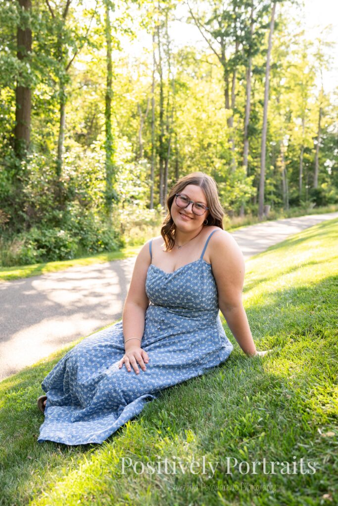 Senior portraits of Tabitha in a blue floral dress on a tree-lined path at Brunswick Lake, golden sunlight filtering through the leaves.
